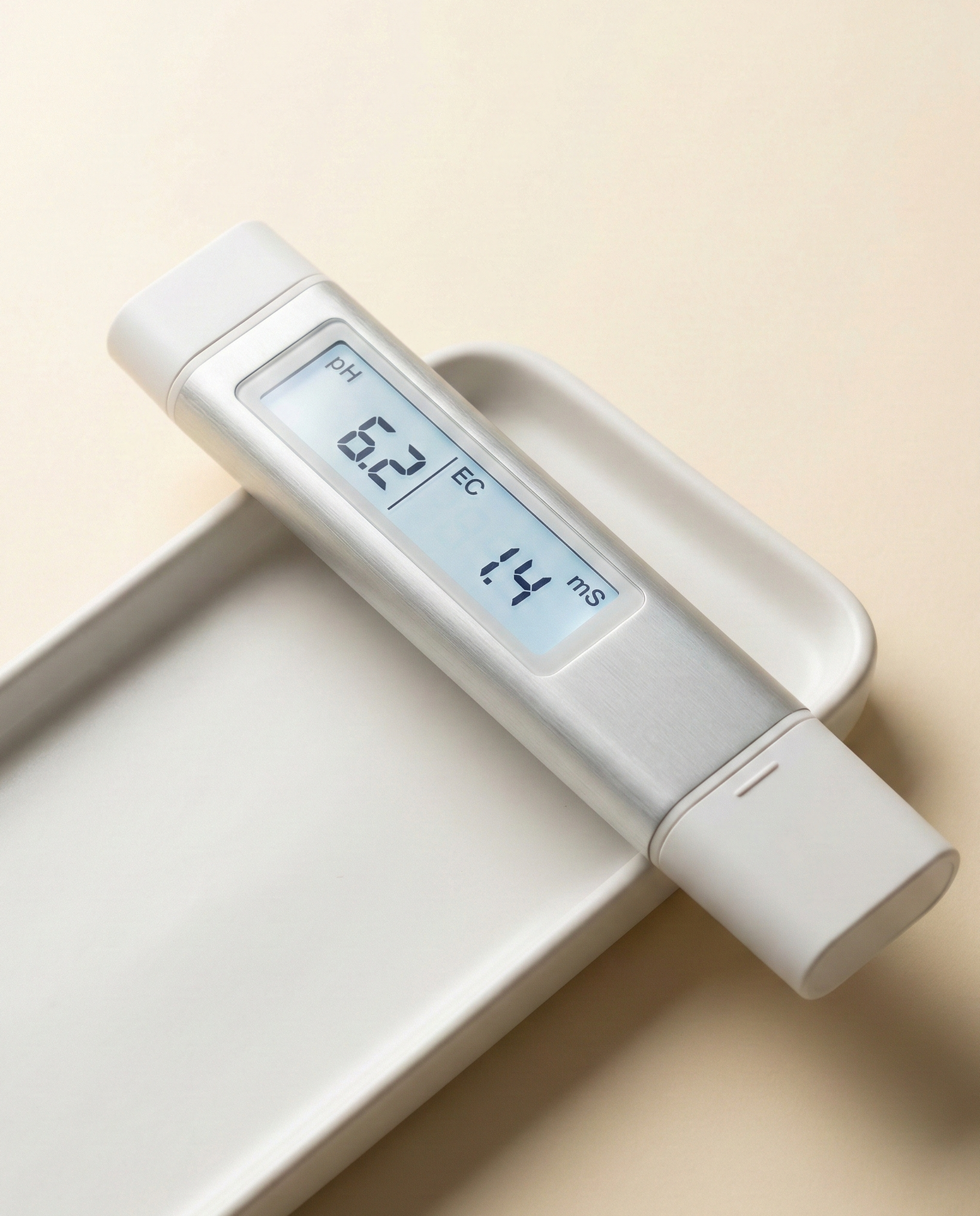 A sleek digital hydroponic pH and EC meter resting on a white ceramic tray.